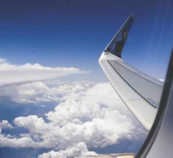 high angle photograph of airplane wings above the clouds under clear blue sky
